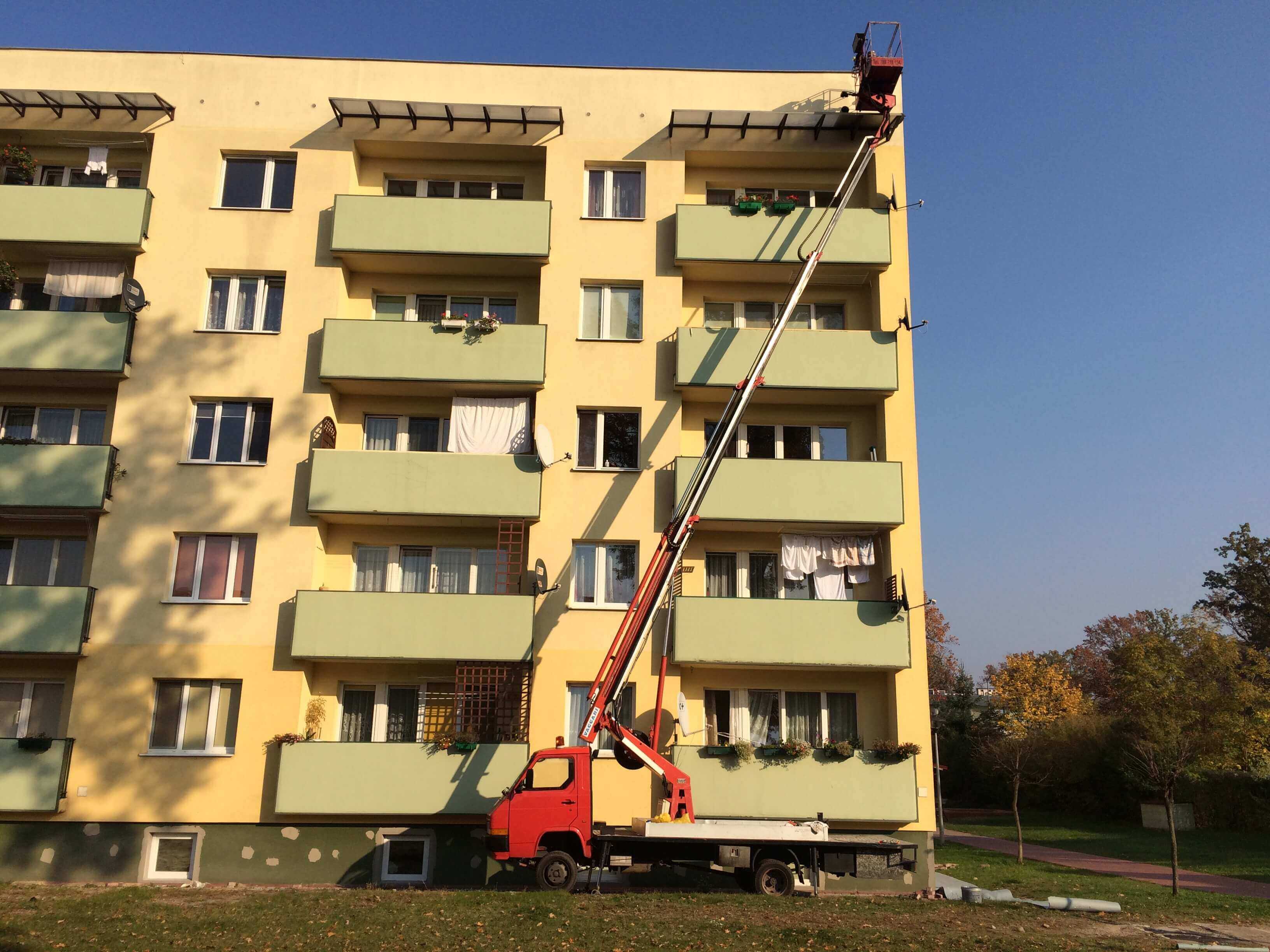 Zwyżka stojąca przy bloku mieszkalnym, operator w koszu na wysokości dachu